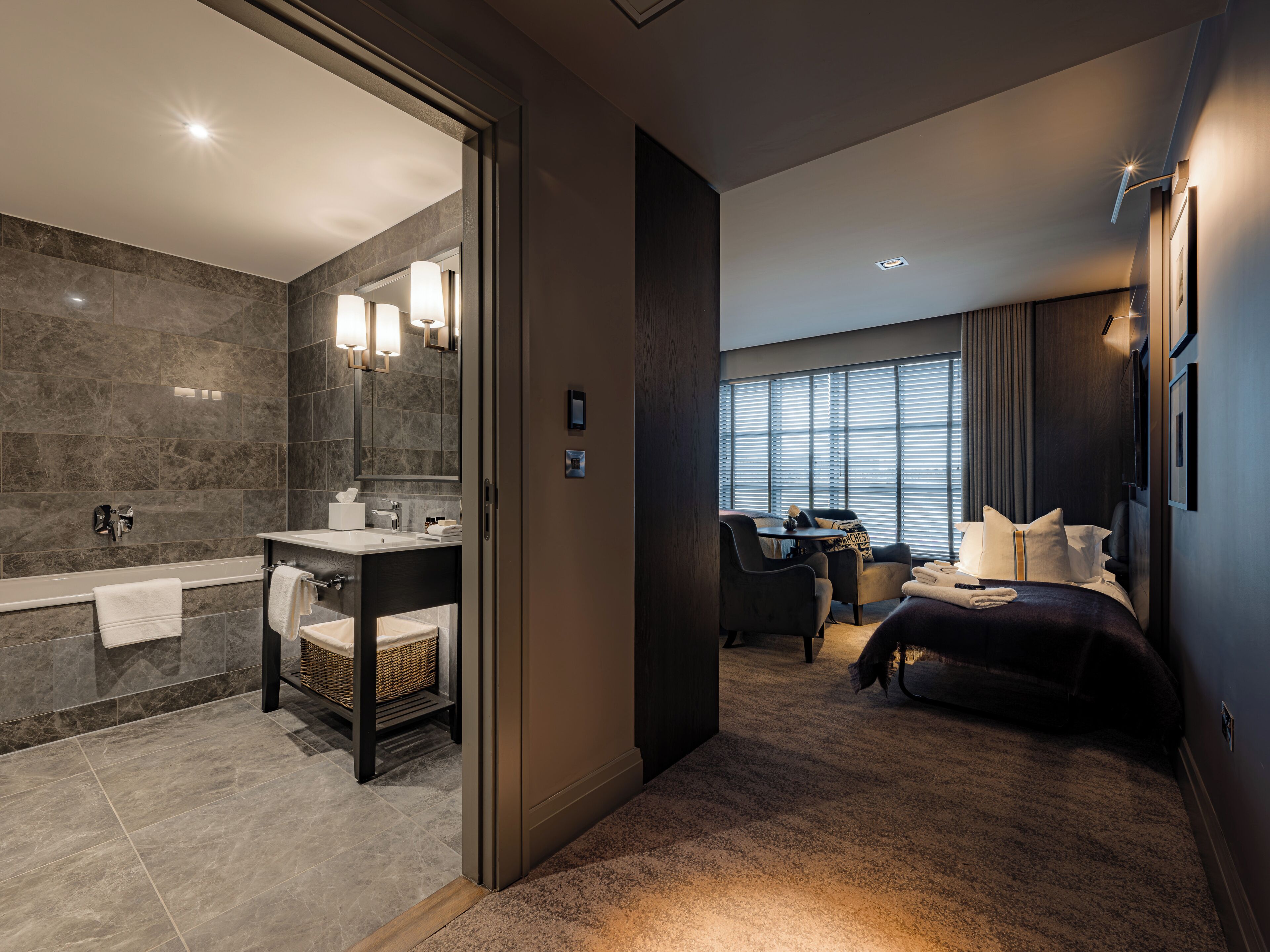 A modern hotel room with a bathroom, a desk, and a bed.