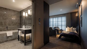 A modern hotel room with a bathroom, a desk, and a bed.