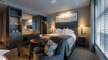 Ein Hotelzimmer mit Bett, Schreibtisch, Stuhl, einem kleinen Tisch, einem Spiegel und einem Fenster mit Jalousien.