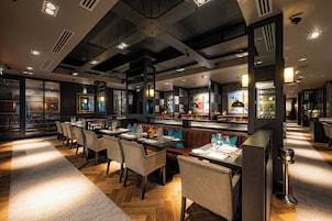 A modern restaurant interior with multiple dining tables, booths, and a bar area.