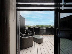 En balkon med fletmøbler, en glasdør og udsigt til himlen og fjerne bygninger.