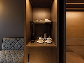 Una kitchenette compacta con cafetera, dos tazas y una pequeña estantería con frascos.