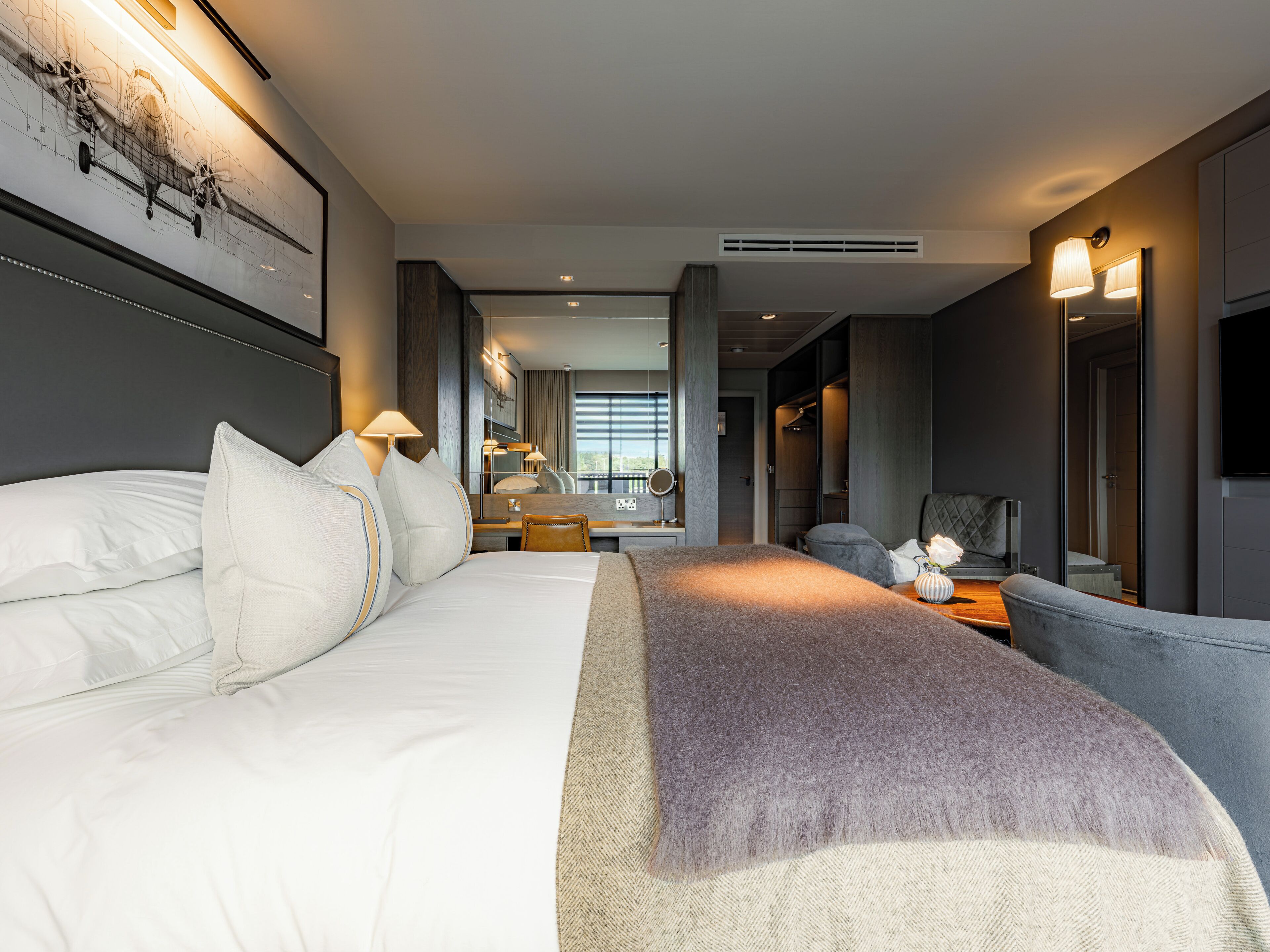 Moderni hotellihuone, jossa on suuri sänky, työpöytä, tuoli, peili ja televisio.