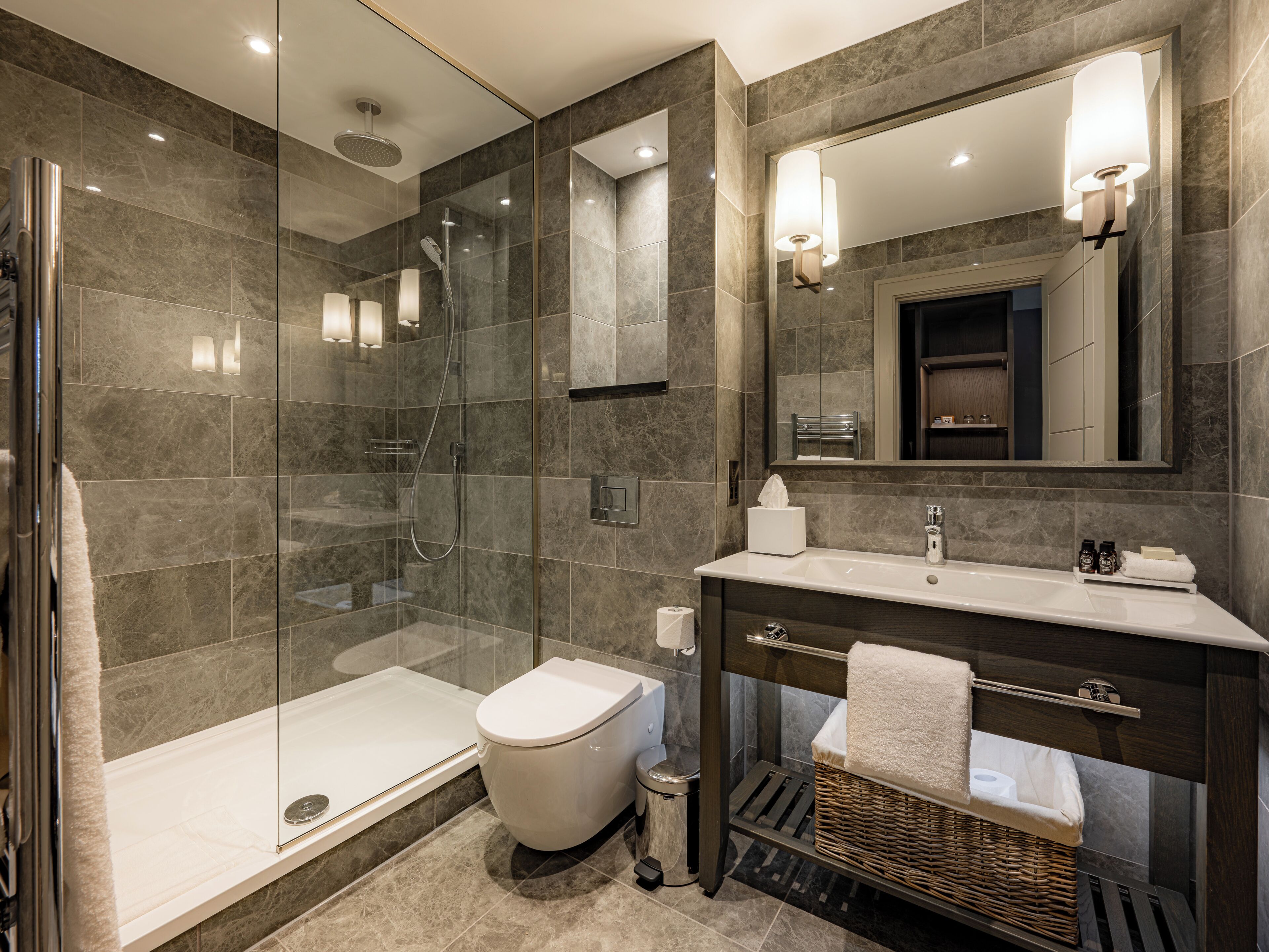 Un baño moderno con cabina de ducha de vidrio, inodoro blanco y tocador con espejo.