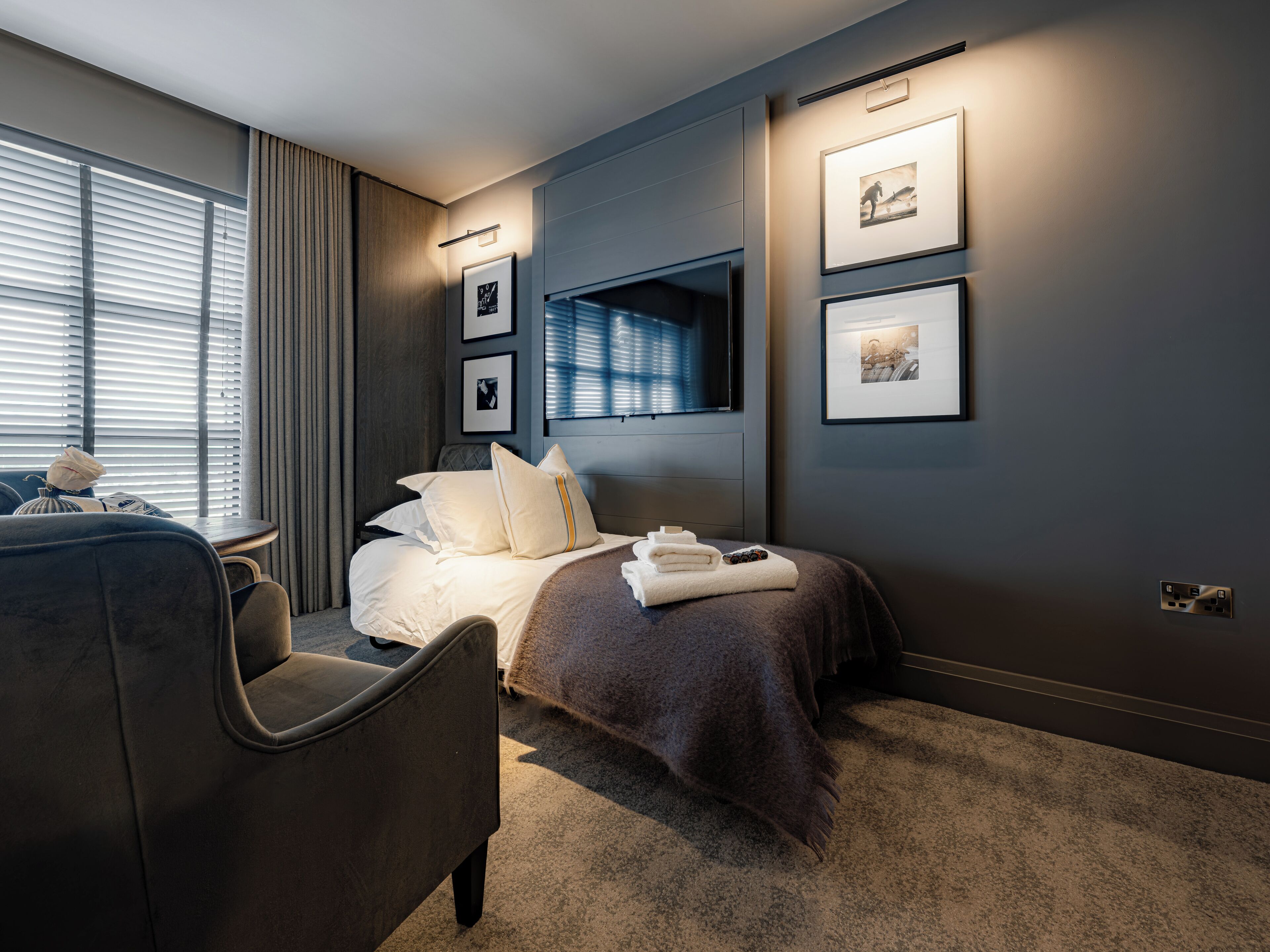 A modern hotel room with a bed, a seating area, and a TV mounted on the wall.