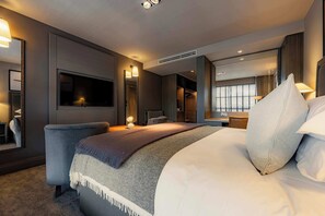 Una habitación de hotel moderna con una cama grande, un área de descanso, un armario y un televisor.