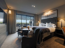 Habitación de hotel moderna con una cama grande, un escritorio, una silla, una mesita y vistas al exterior a través de amplios ventanales.