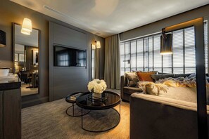 A modern living room with a sofa, a round coffee table with a vase, a flat-screen TV, and a large window with blinds. - Dakota Manchester Airport (Manchester)