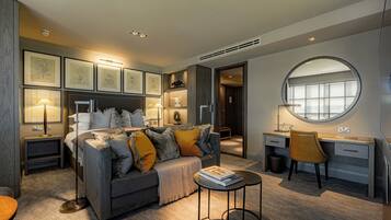 A modern bedroom with a grey sofa, a round mirror, a desk, and framed artwork on the walls.