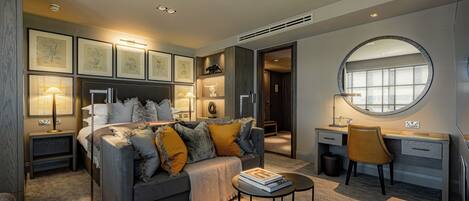 A modern bedroom with a grey sofa, a round mirror, a desk, and framed artwork on the walls.