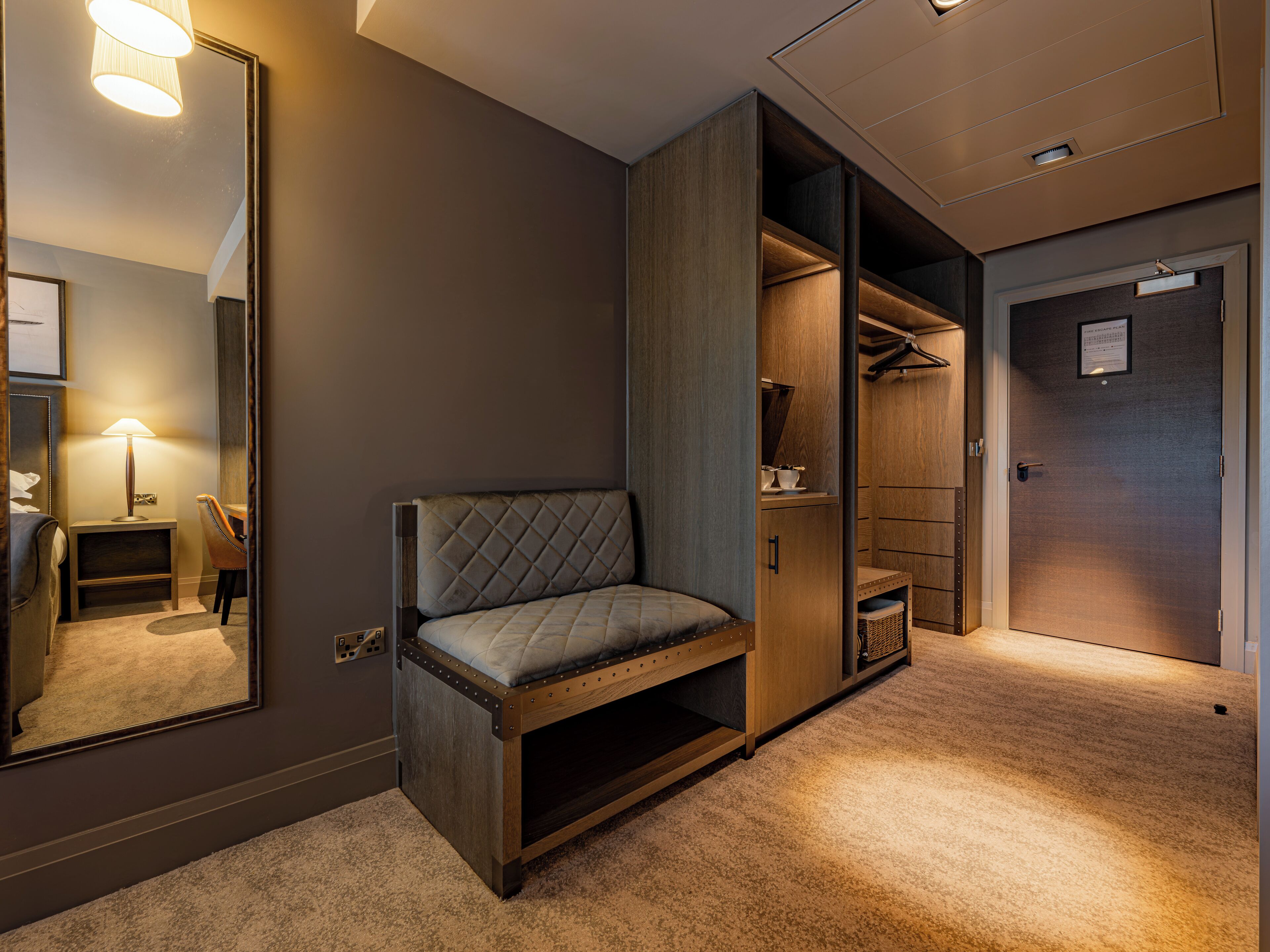 A hotel room with a bed, a seating area, a wardrobe, and a mirror.