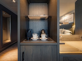A compact hotel room with a kitchenette, a bed with white linens, and a view of the cityscape.