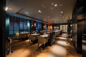Interior moderno de restaurante con piso de madera, mesas dispuestas para comer y una zona de bar.