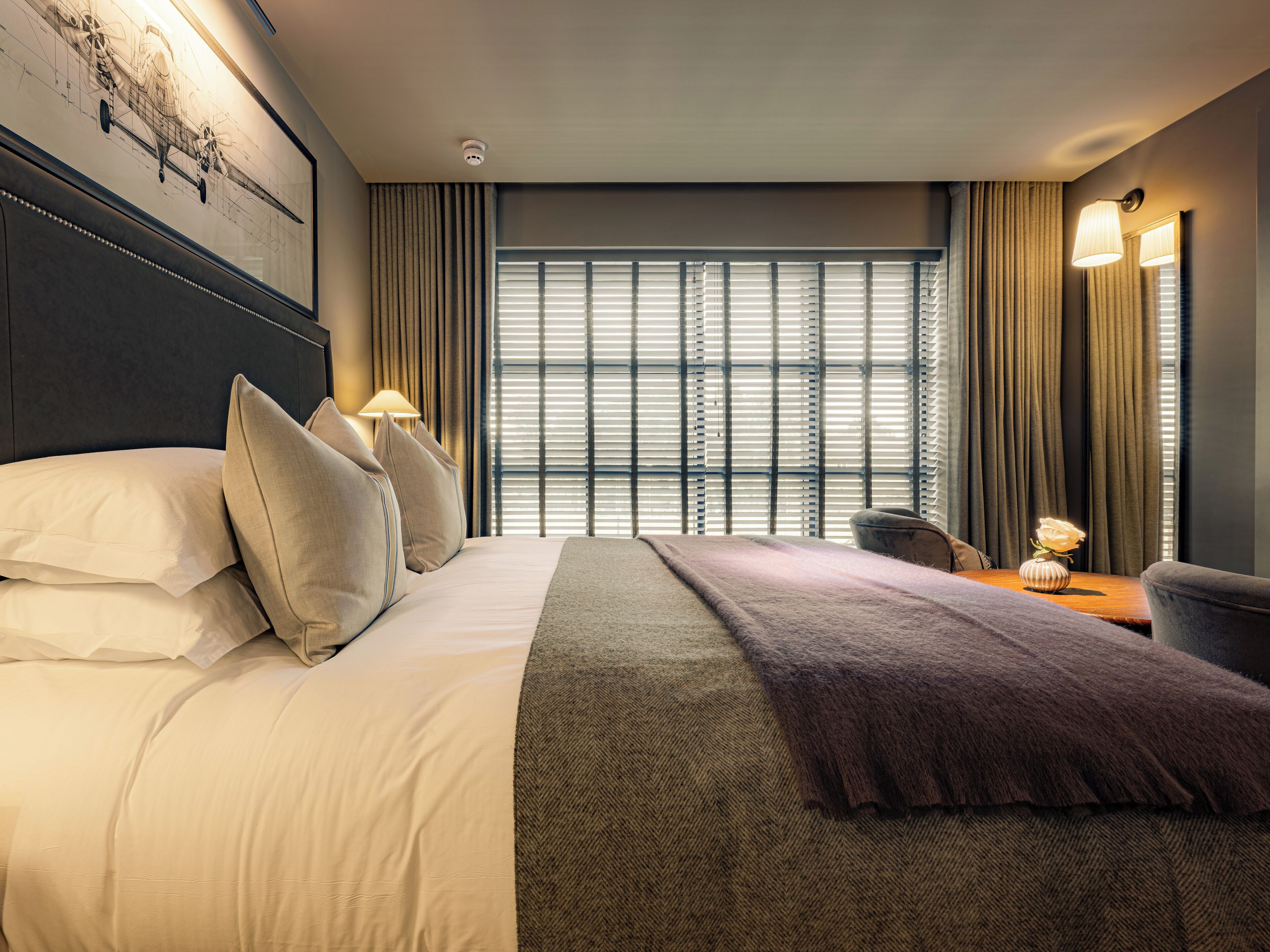 A hotel room with a large bed, a desk, and a window with blinds.