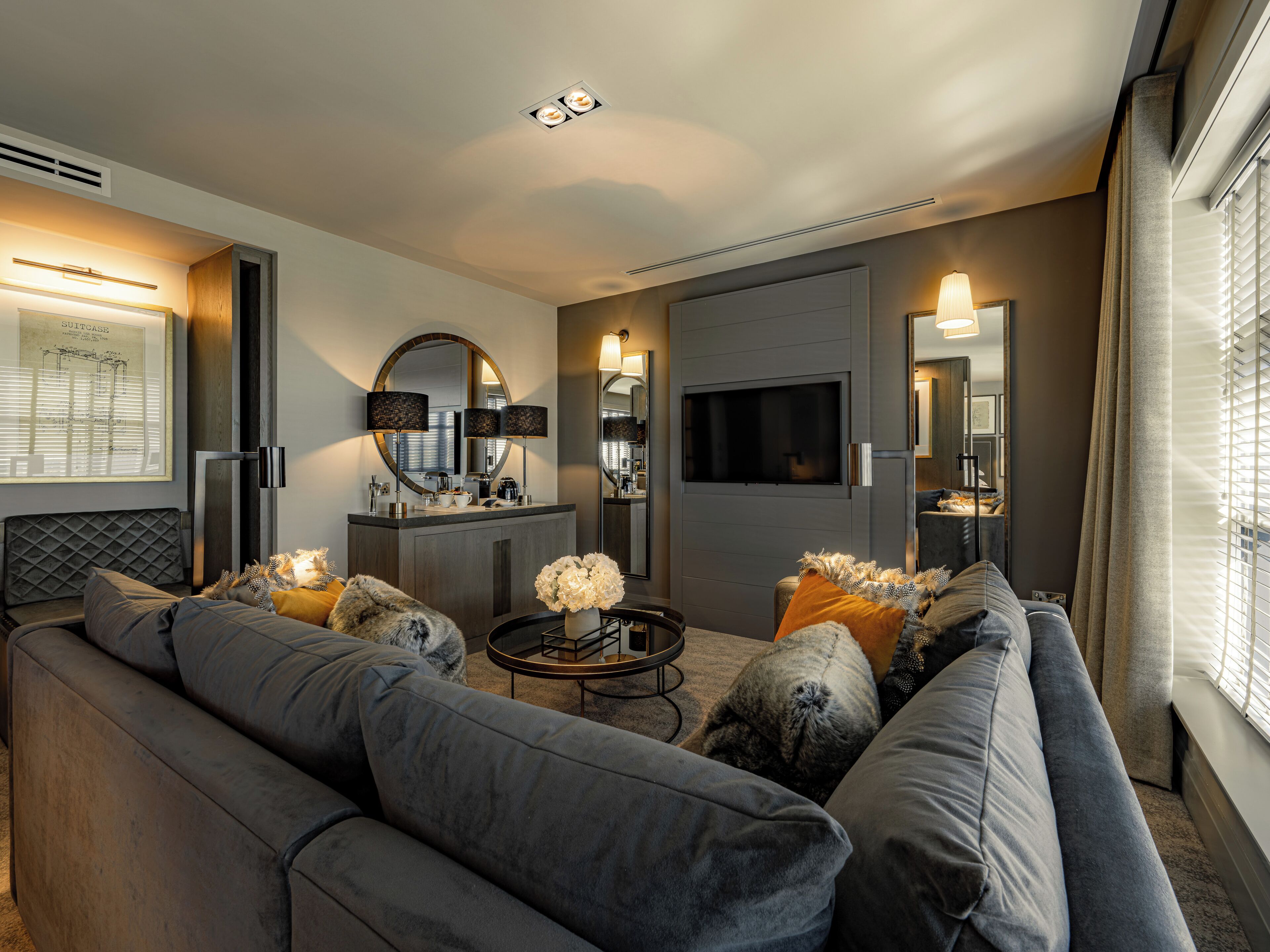 A modern living room with a grey sofa, a coffee table, and a flat-screen TV mounted on the wall.