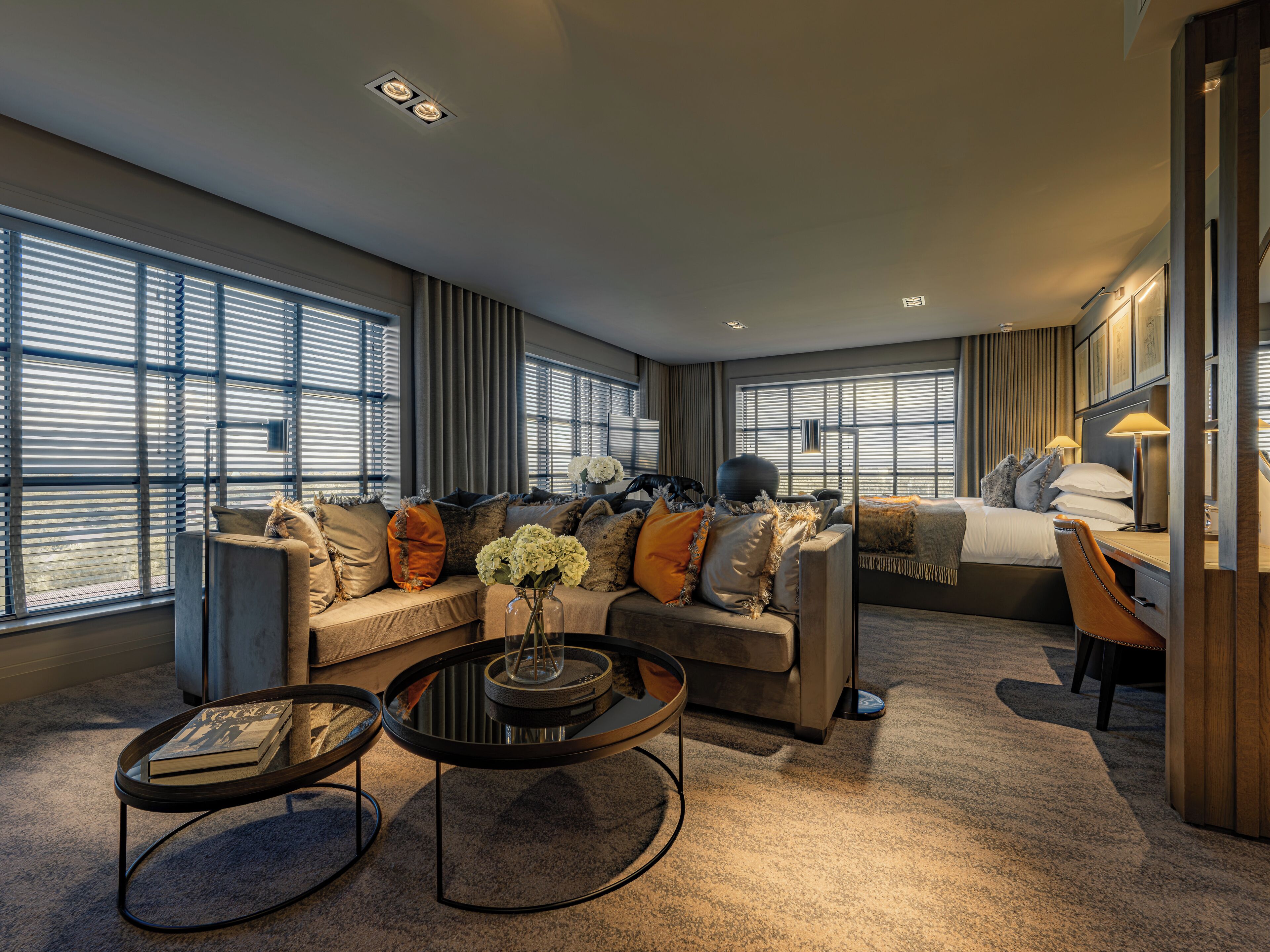 A modern hotel room with a sofa, a round coffee table, a bed, and a desk area.