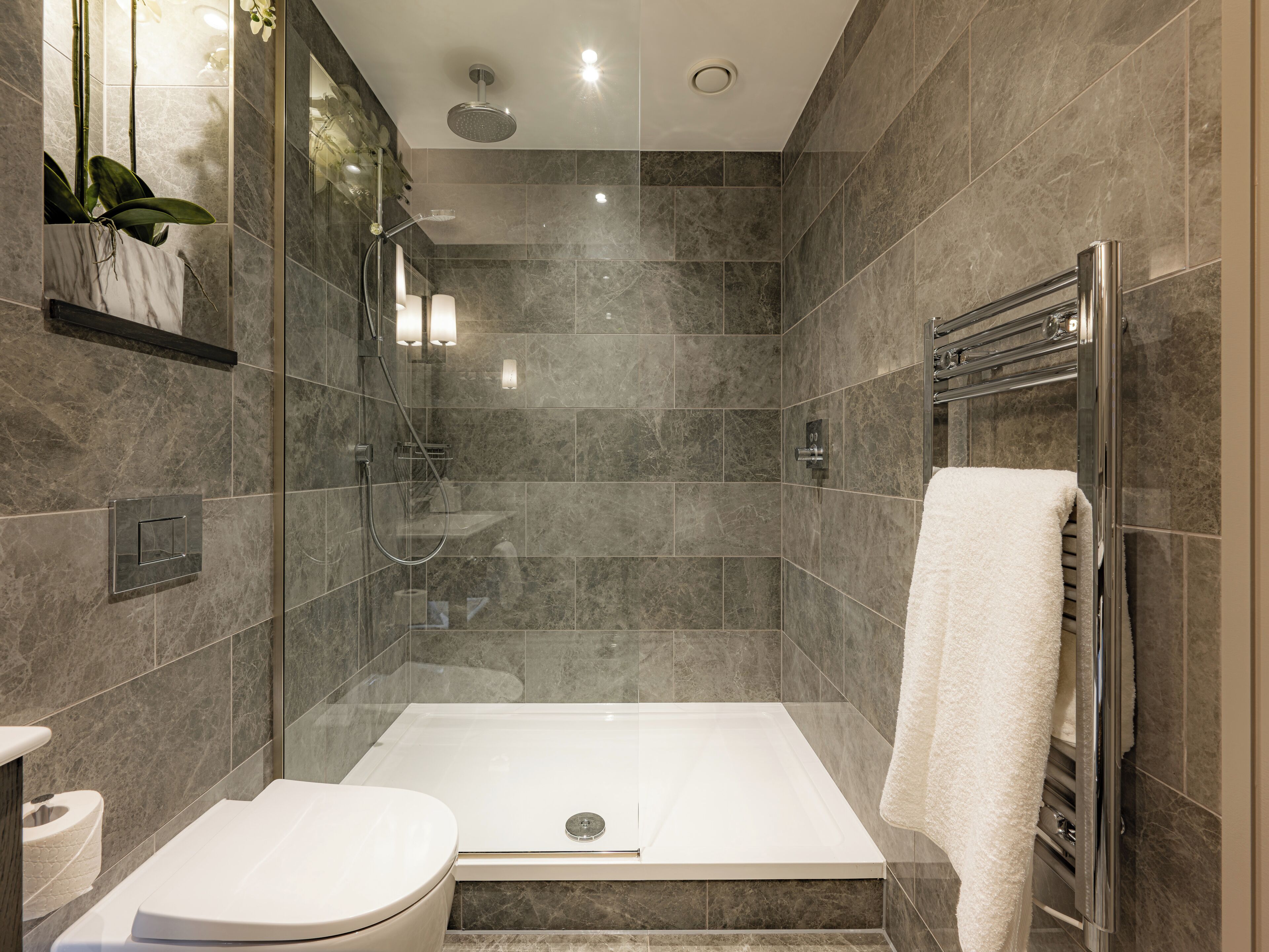 A modern bathroom with a glass-enclosed shower, a white toilet, and a towel rack.