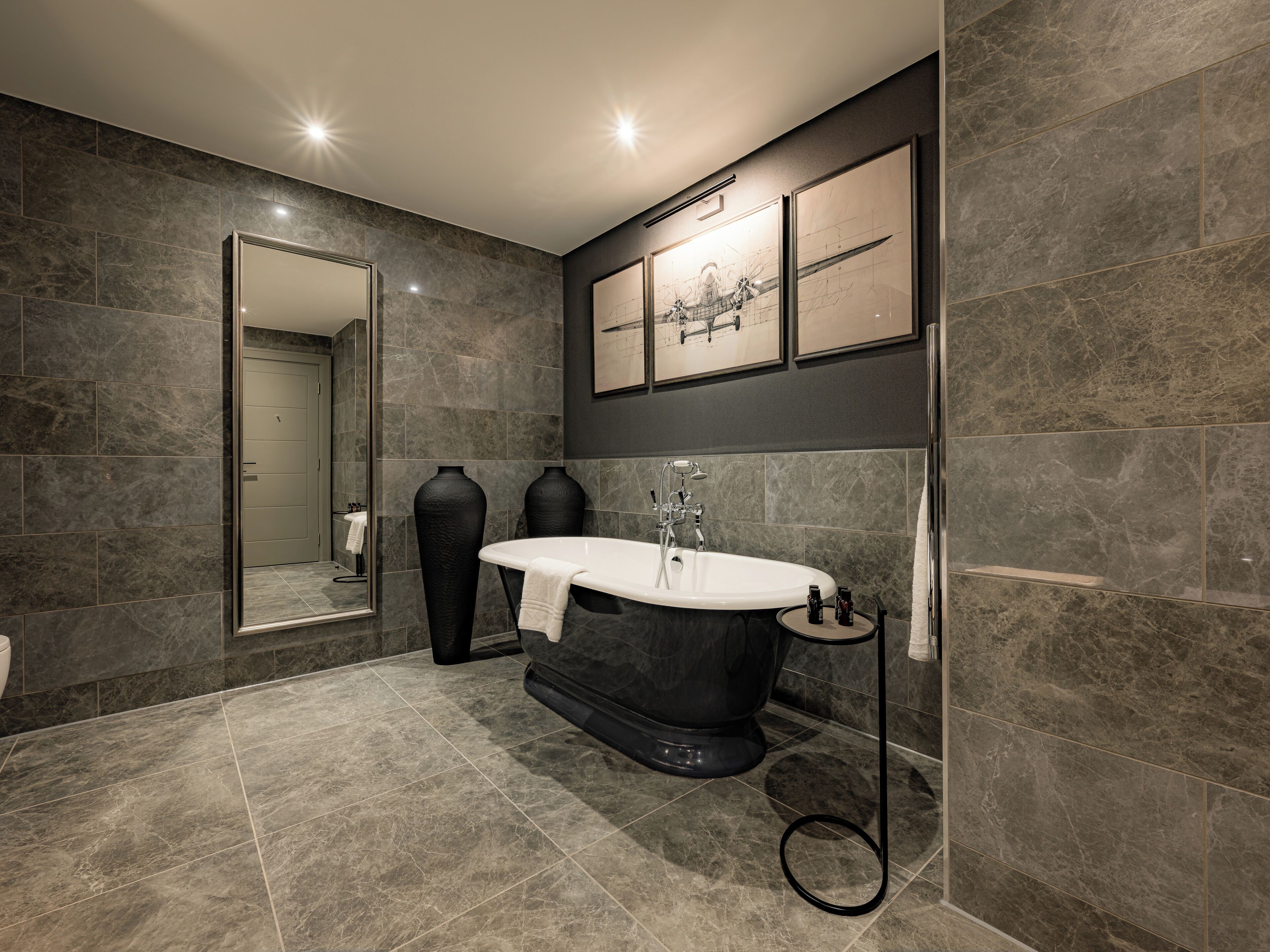 Un baño moderno con una bañera independiente, un espejo grande y una obra enmarcada sobre el lavabo.