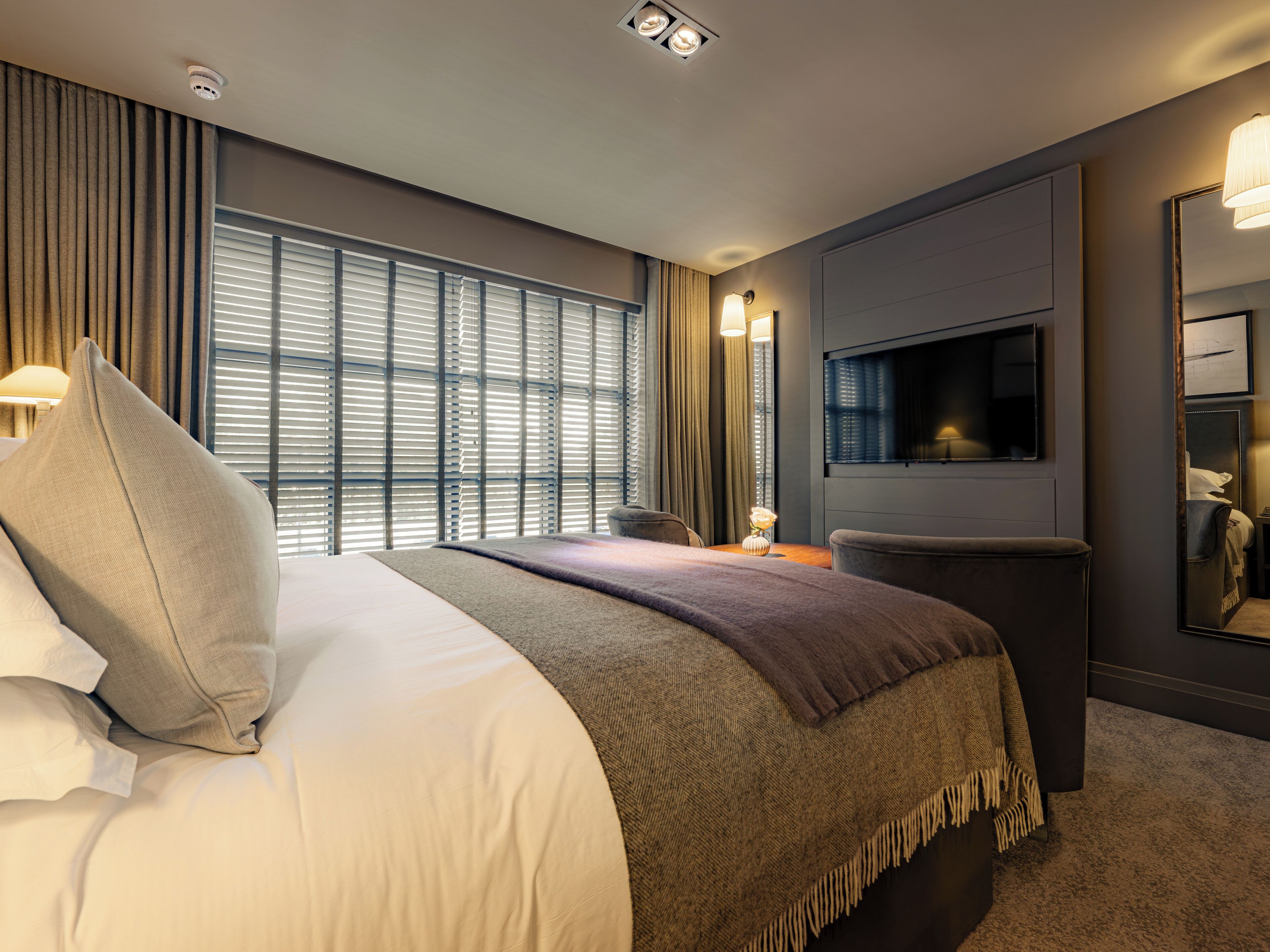Une chambre d’hôtel avec un grand lit, un téléviseur fixé au mur et une fenêtre avec des stores.