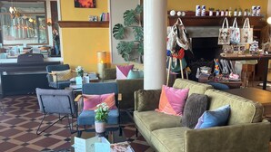 A cozy lobby with a checkered floor, a green sofa with colorful cushions, a coffee table with a magazine, and a large mirror reflecting the room. - hôtel boutique la maison des galets (Saint-Valery-en-Caux)