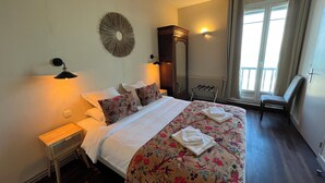 A neatly made bed with floral bedding, a small bedside table, and a wall-mounted decorative item. - hôtel boutique la maison des galets (Saint-Valery-en-Caux)
