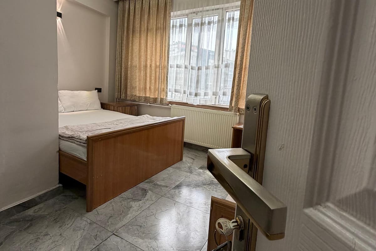 Hotellihuone, jossa on sänky, työpöytä, ikkuna verhoilla ja patteri.