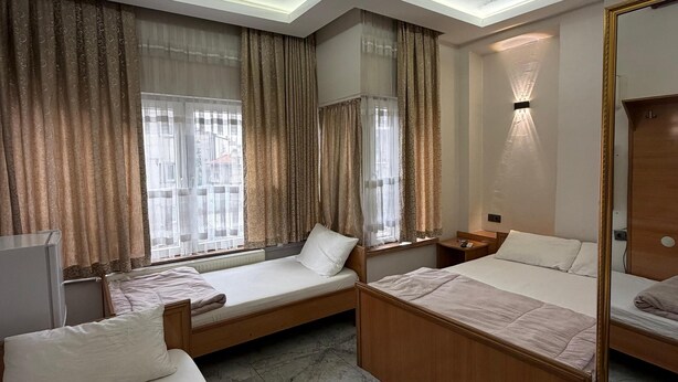 A hotel room with two beds, a desk, a mirror, and a window with curtains. - Hotel KONAK (Gaziantep)