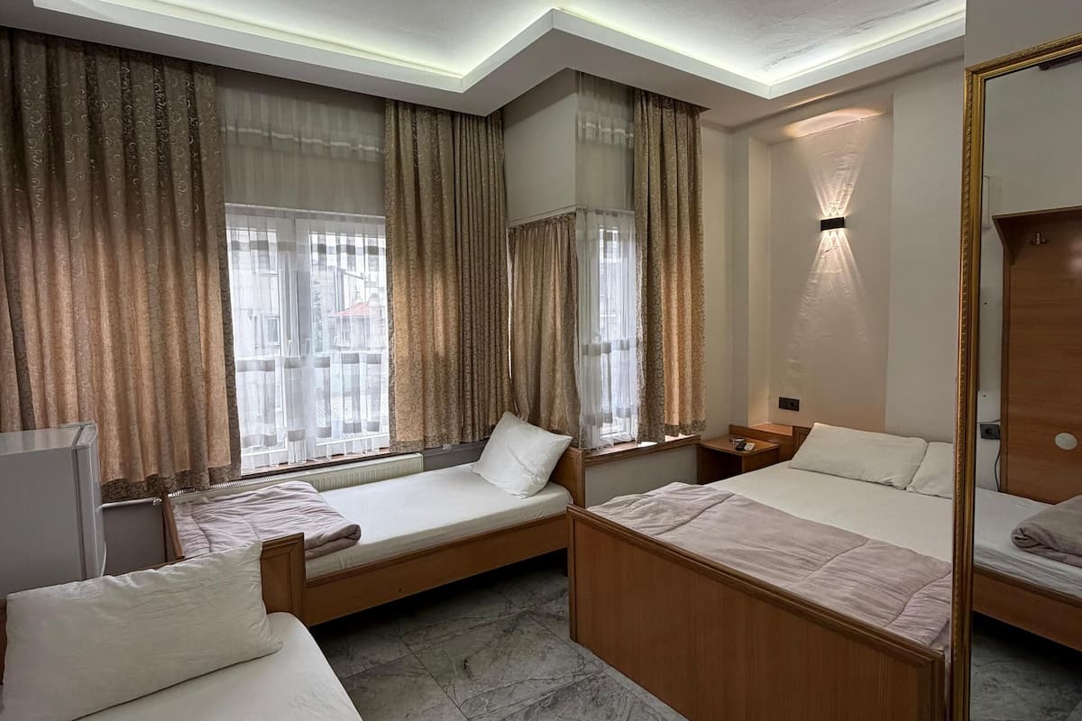Hotellihuone, jossa on kaksi sänkyä, työpöytä, peili ja ikkuna, jossa on verhot.
