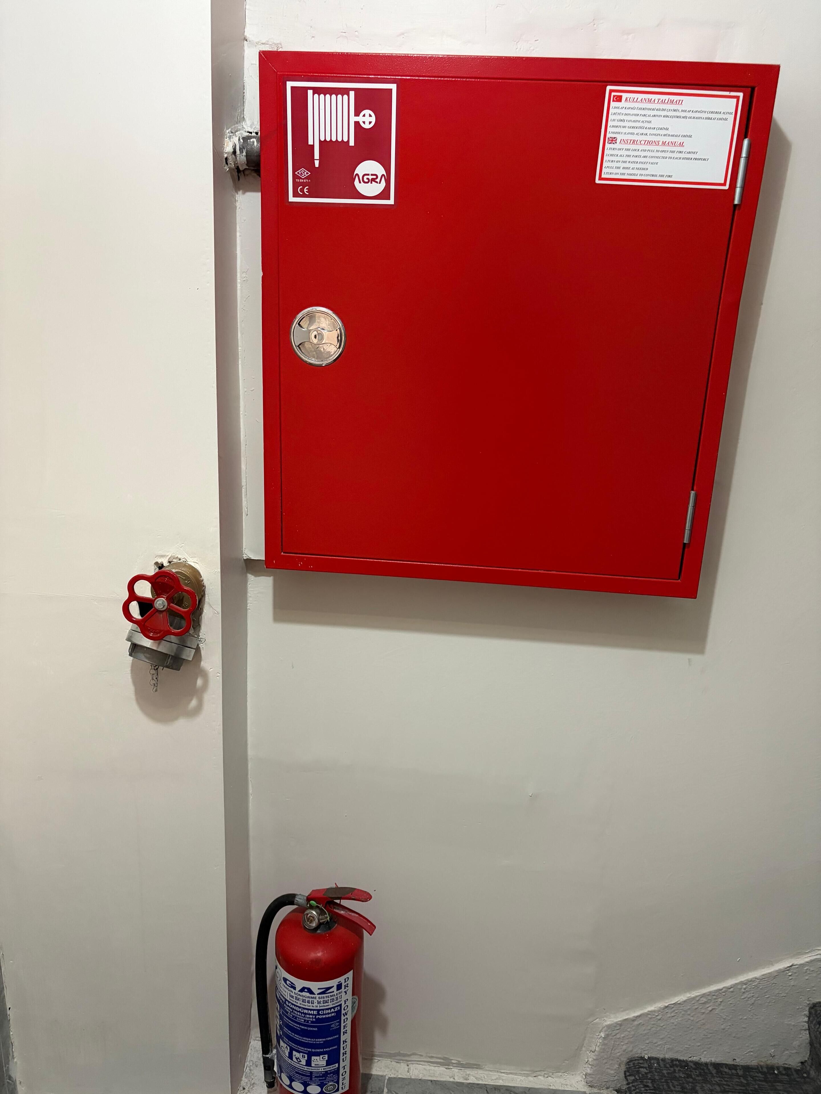 A red fire alarm box with a manual pull station and a fire extinguisher mounted on the wall.