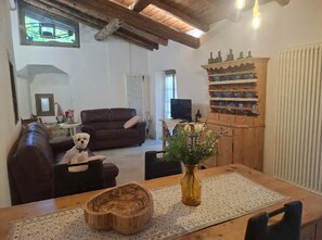 Una sala de estar acogedora con un sofá de cuero marrón, una mesa de comedor de madera con un florero y un aparador de madera con vajilla.