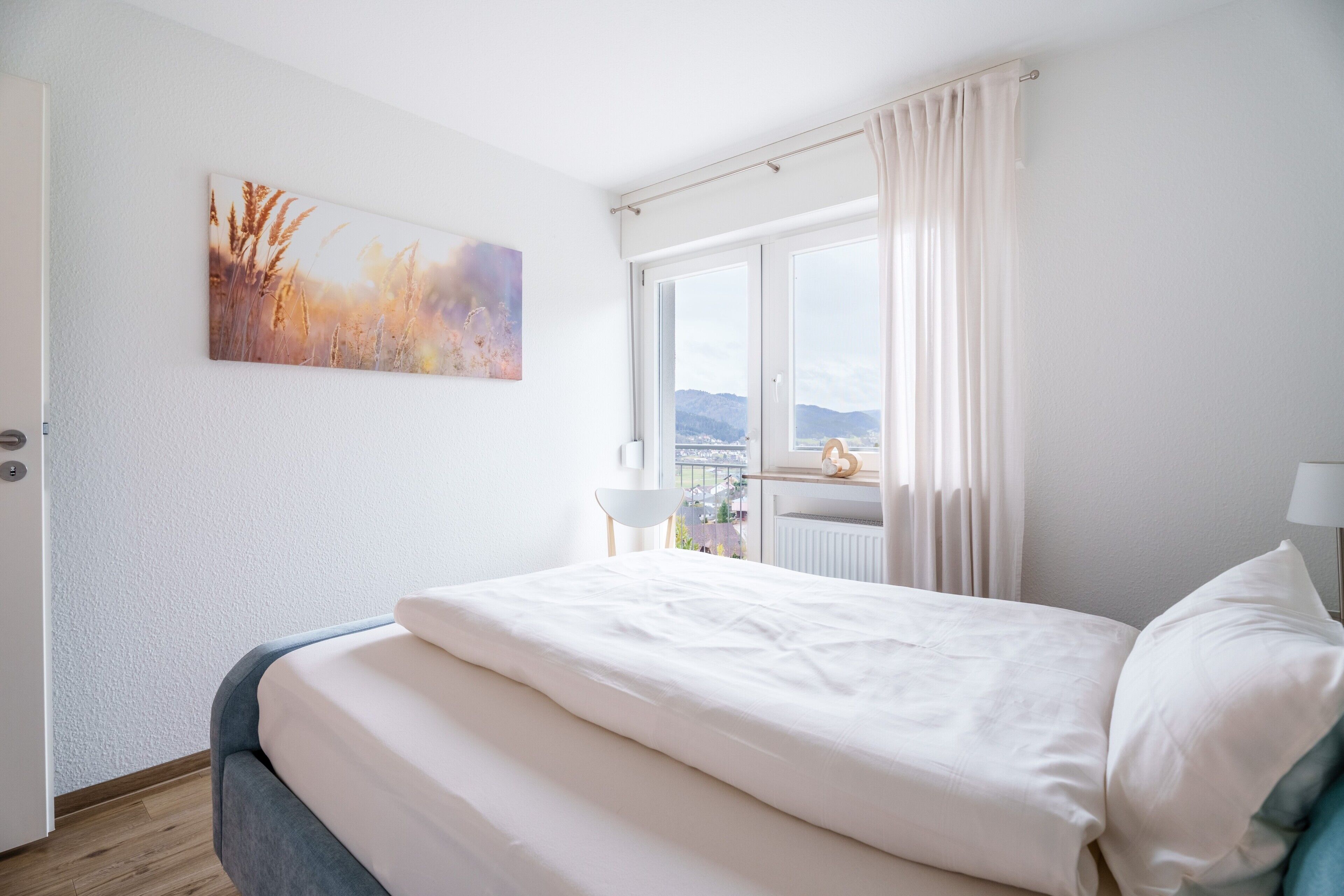 Een slaapkamer met een bed, een raam met gordijnen, een lamp en een schilderij aan de muur.