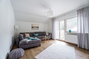 En moderne stue med en grå sofa, en rund skammel, en hvid måtte og et vindue med gardiner.