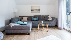 Een moderne woonkamer met een hoekbank, een glazen salontafel en uitzicht door een groot raam.