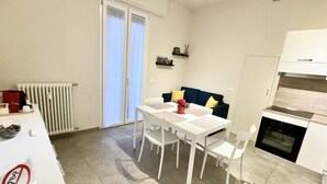 Un espace de vie compact comprenant un coin repas, une kitchenette et une porte-fenêtre coulissante donnant sur un balcon.