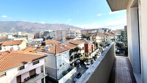 Un balcon offrant une vue sur le paysage urbain, avec des bâtiments aux toits recouverts de tuiles rouges et une chaîne de montagnes lointaine.