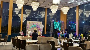 A spacious indoor venue with high ceilings, chandeliers, and a stage with a neon 'A' backdrop. Tables and chairs are arranged for guests. - SK PREMIUM PARK SONIPAT (Ganaur)
