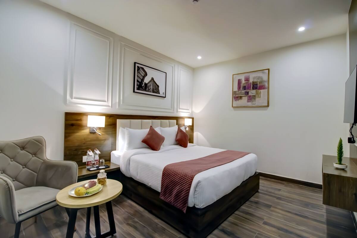 A hotel room with a bed, a chair, a small table with a fruit plate, and a nightstand with a lamp.