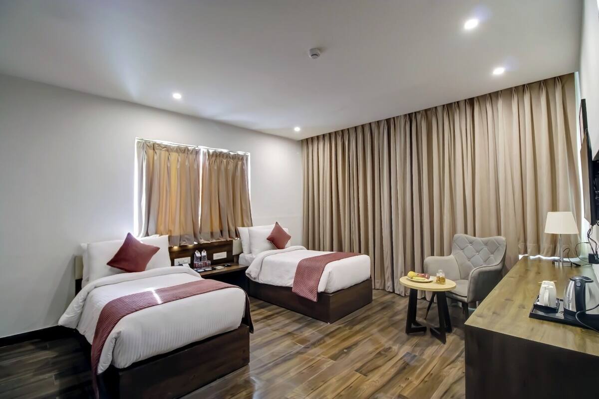 A hotel room with two beds, a desk, a chair, and a large window with curtains.