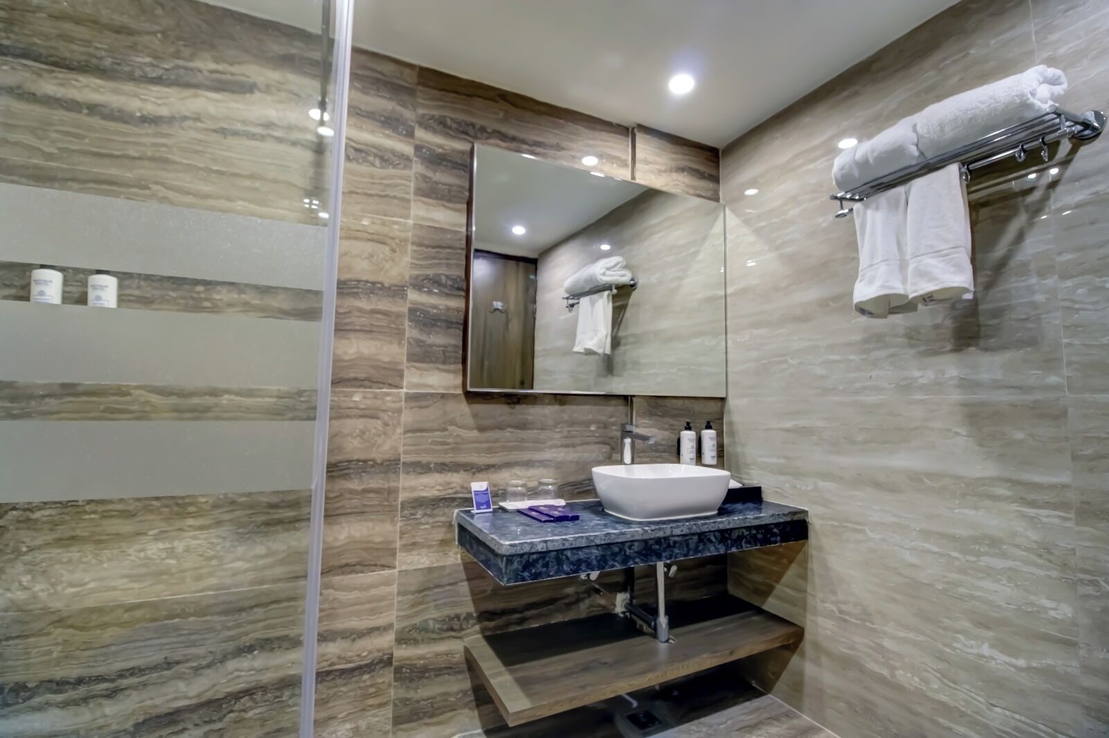 A modern bathroom with a marble wall, a large mirror, a sink with a marble countertop, and a towel rack.