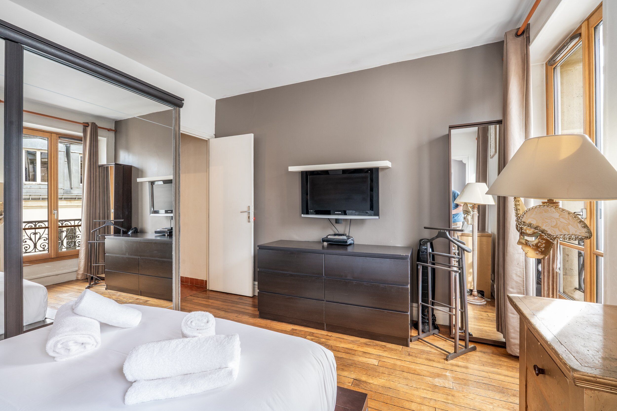 Une chambre d’hôtel avec un lit, une télévision, une commode, un miroir et une vue sur le balcon.