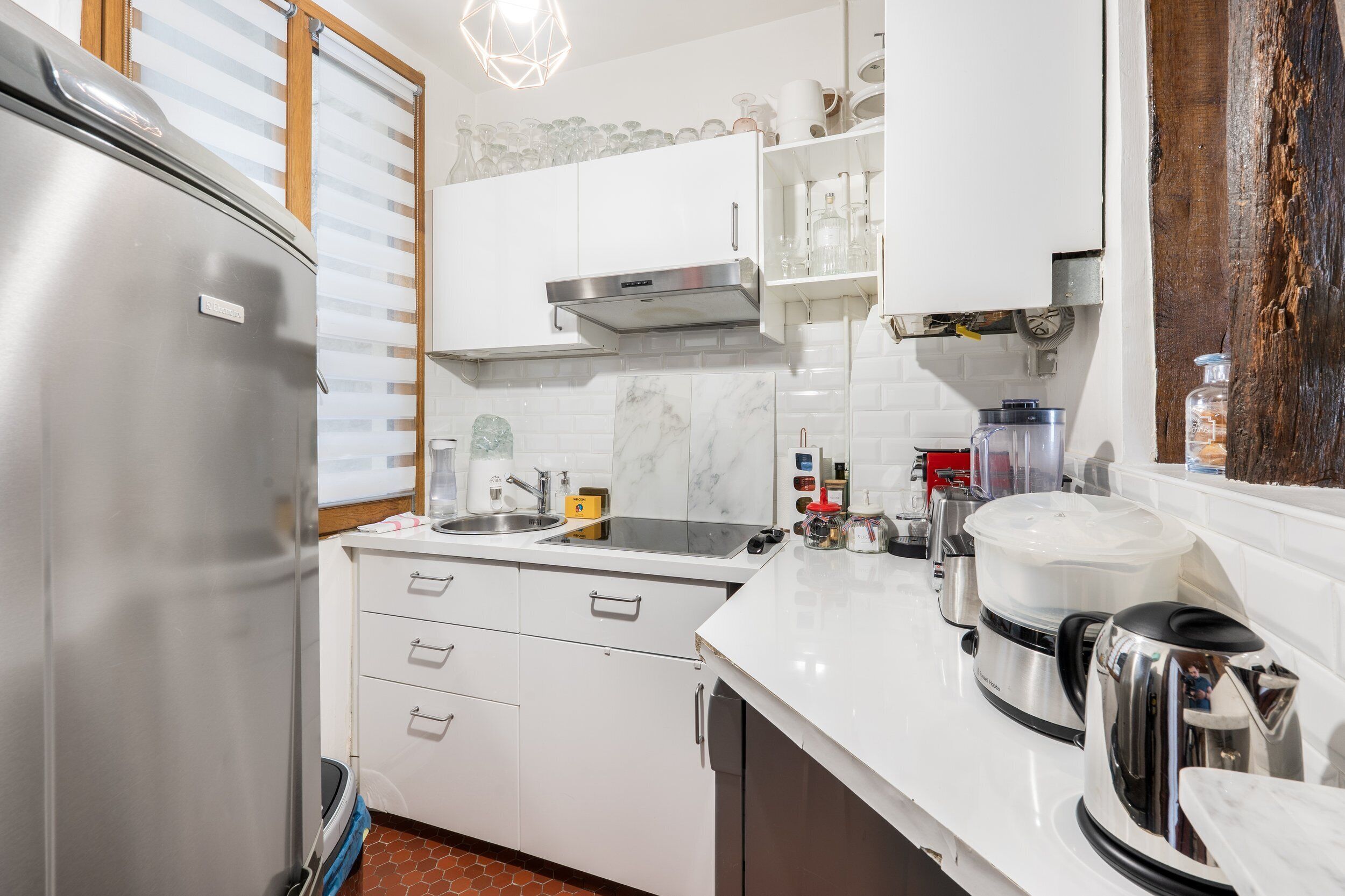 A modern kitchen with white cabinets, a stainless steel refrigerator, a sink, and various appliances including a coffee maker and a kettle.