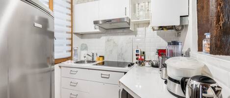 A modern kitchen with white cabinets, a stainless steel refrigerator, a sink, and various appliances including a coffee maker and a kettle.