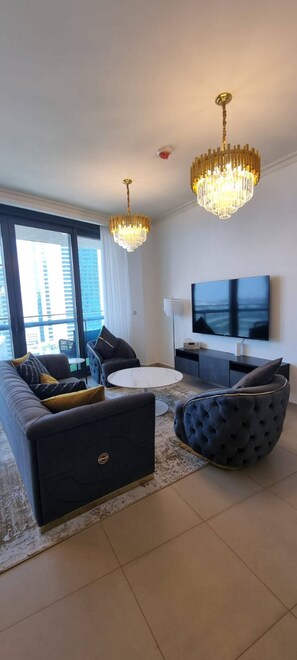 Ein modernes Wohnzimmer mit Sofa, Sessel und rundem Couchtisch. An der Wand ist ein Flachbildfernseher angebracht und von der Decke hängt ein Chandelier.