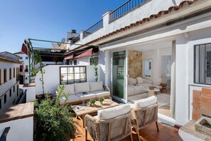 Un amplio patio con un sofá, sillas de mimbre y una mesa, con vistas a un paisaje urbano.