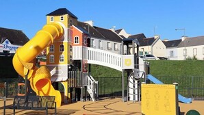 Un parque infantil con un tobogán amarillo y estructuras para escalar, rodeado de edificios residenciales.