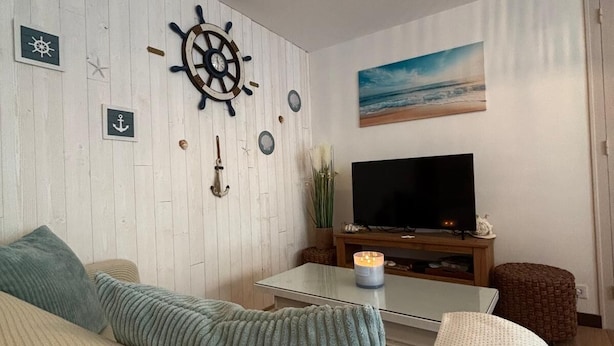 Un salón con televisor, decoración de pared de madera y un cuadro de una playa.