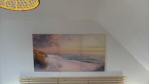 Un dormitorio con una cama grande, cabecera de madera, dos mesitas de noche con lámparas y un cuadro con una playa en la pared.