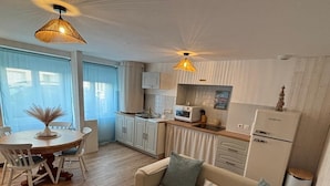 Una cocina moderna con armarios blancos, un microondas y un refrigerador. Hay un comedor con una mesa y sillas, y una sala de estar con un sofá y una mesita de centro.