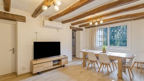 A modern living room with a flat-screen TV, wooden dining table, chairs, and exposed wooden beams. - Holiday Home 'La Caseta De L'Adela' with Mountain View, Wi-Fi and Air Conditioning (Arbúcies)