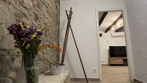 A room with a stone wall, a wooden bench, a vase with flowers, a broom, and a television in the background. - Holiday Home 'La Caseta De L'Adela' with Mountain View, Wi-Fi and Air Conditioning (Arbúcies)